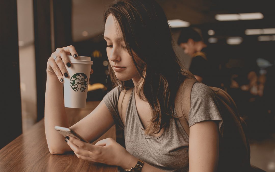 Ragazza che digita su Smartphone seduta da Starbucks